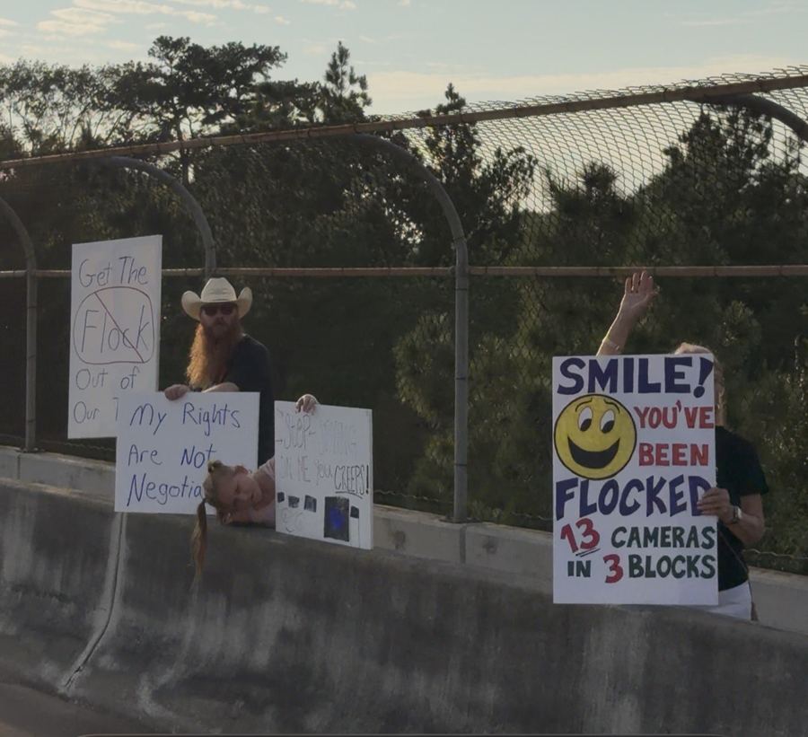 Volunteers on the bridge holding signs, including one reading Smile, you've been Flocked, 13 cameras in 3 blocks